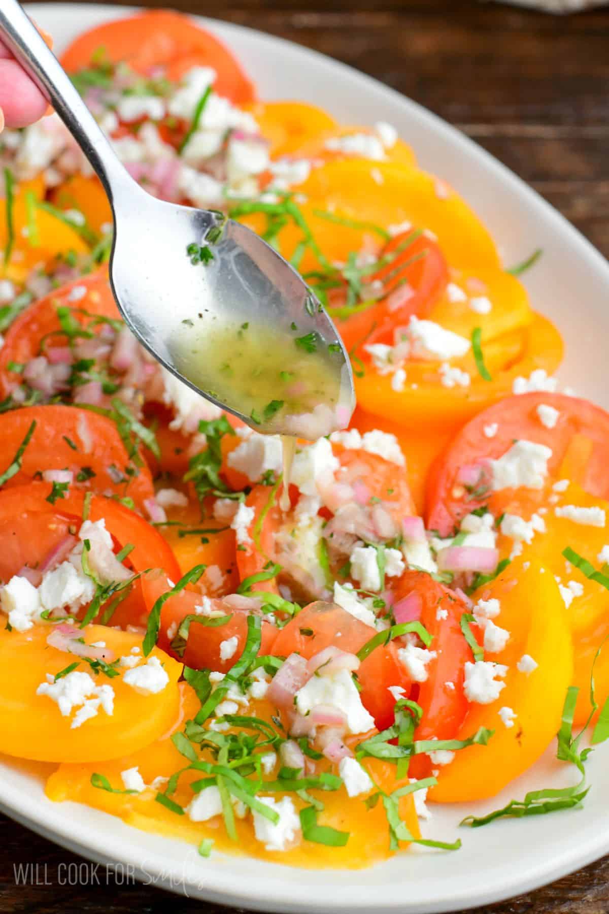 drizzling the shallot vinaigrette over the tomato salad on a platter.