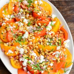 heirloom tomato salad spread on the platter topped with pine nuts, feta, basil, and shallot vinaigrette.