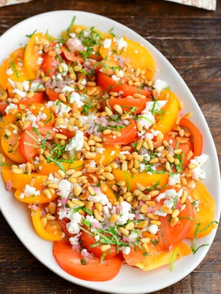 heirloom tomato salad spread on the platter topped with pine nuts, feta, basil, and shallot vinaigrette.