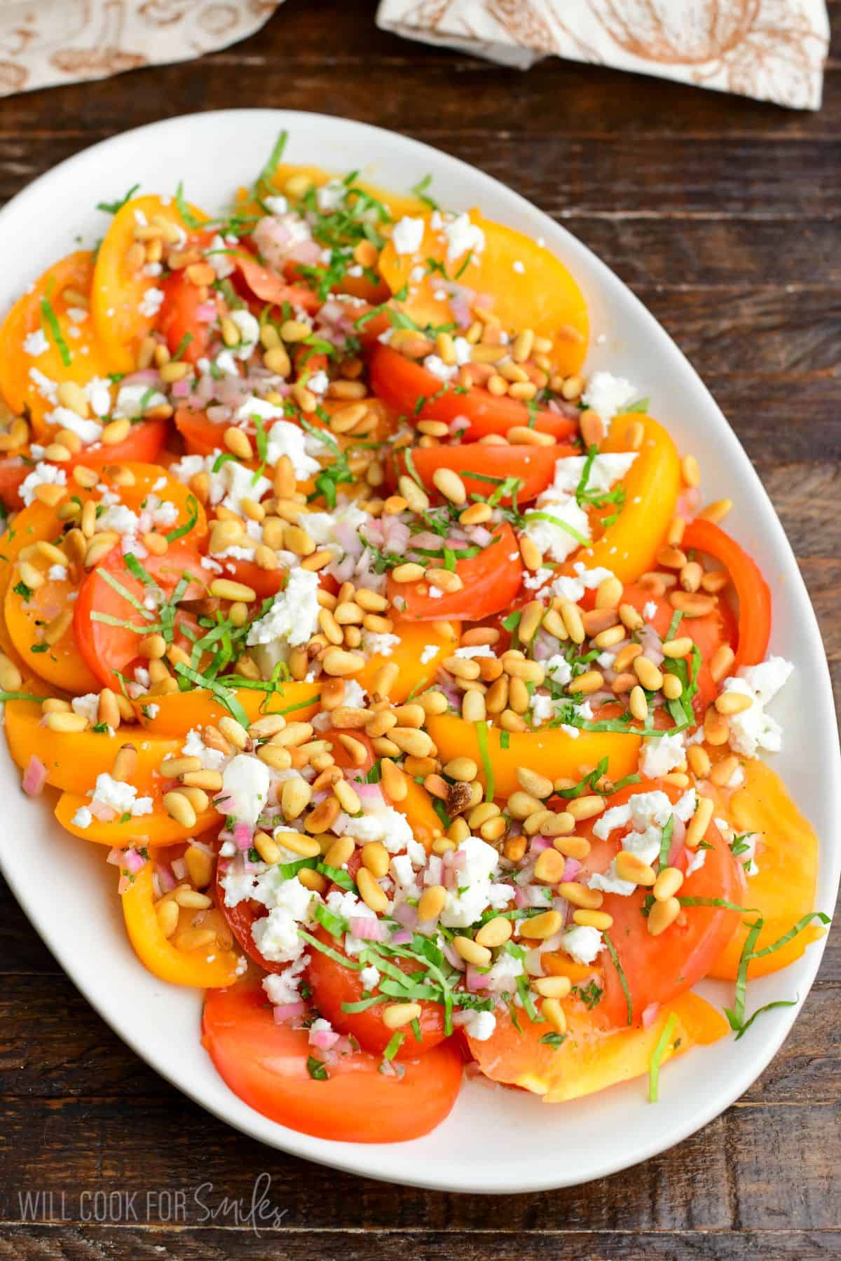heirloom tomato salad spread on the platter topped with pine nuts, feta, basil, and shallot vinaigrette.