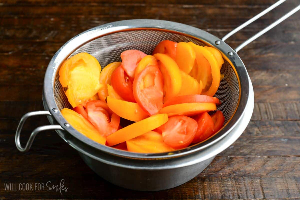 sliced heirloom tomatoes sitting in the mesh strainer with salt to get excess liquid out.