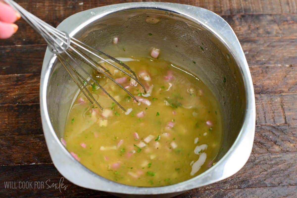 whisking together the ingredients for shallot vinaigrette in a mixing bowl.