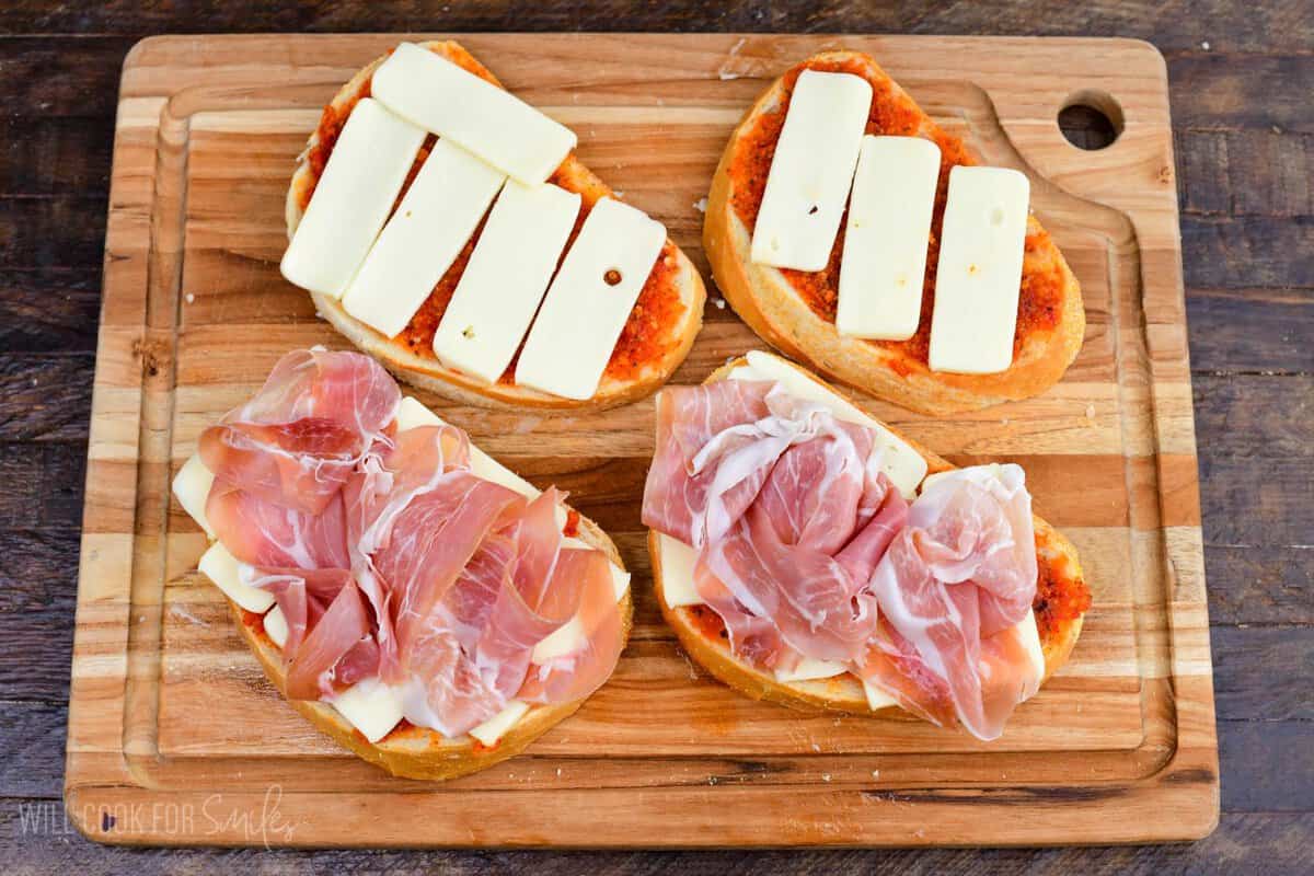 Making Sun Dried Tomato Pesto Grilled Cheese, combining bread, pesto, cheese, and prosciutto.