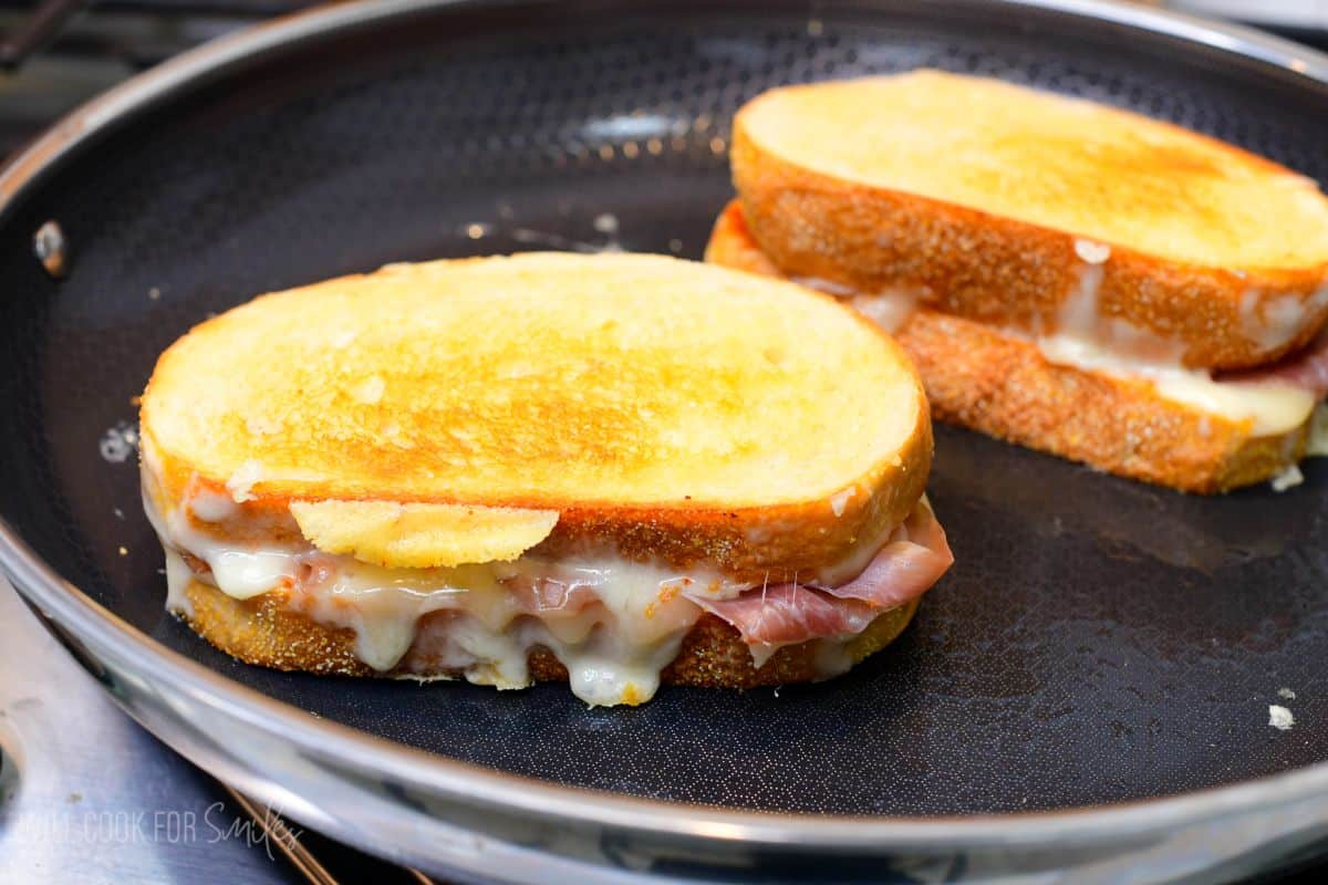 cooked Italian pesto grilled cheese with sun dried tomato pesto, fontina cheese, and prosciutto in a pan.