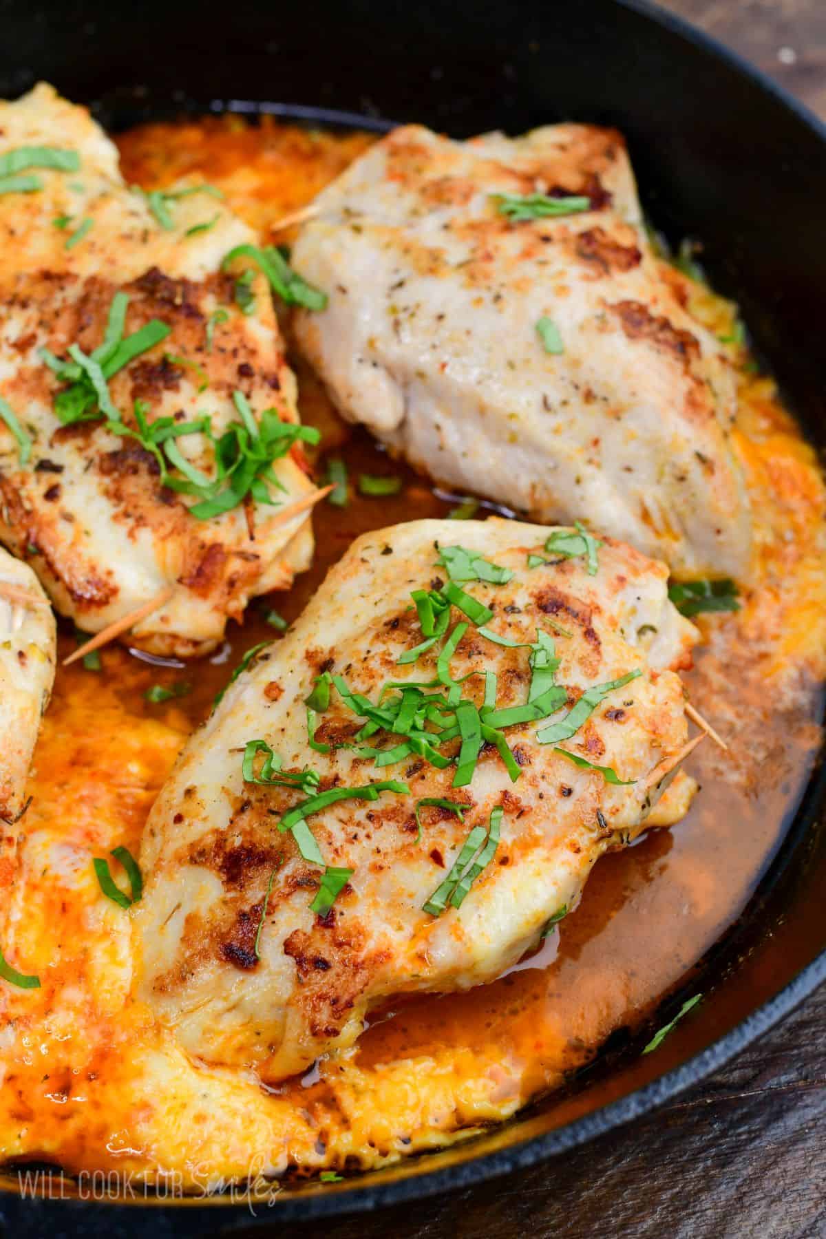 Sun dried tomato pesto stuffed chicken baked in a cast iron skillet with melted cheese and fresh basil as garnish.