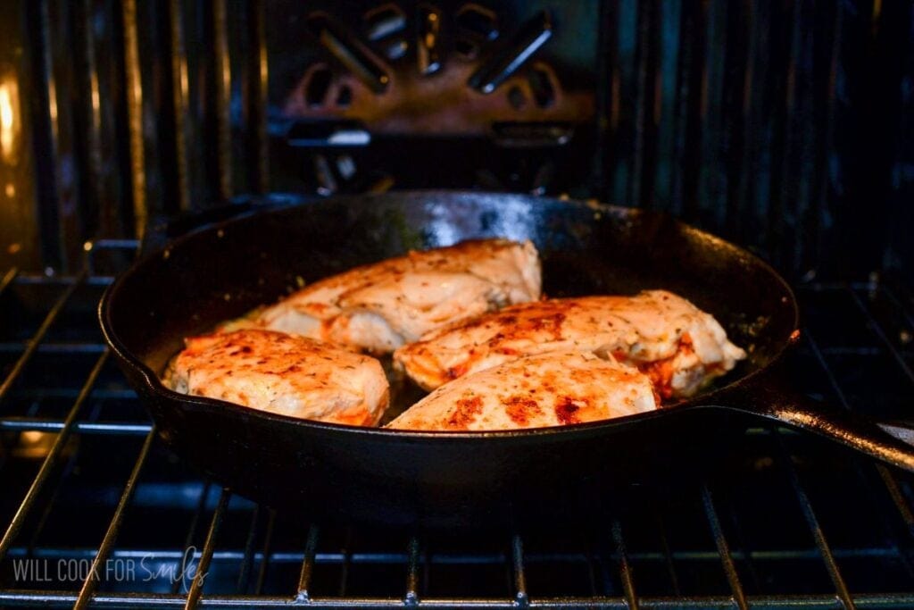 Stuffed chicken breasts baking in a cast iron skillet until golden brown in the oven.