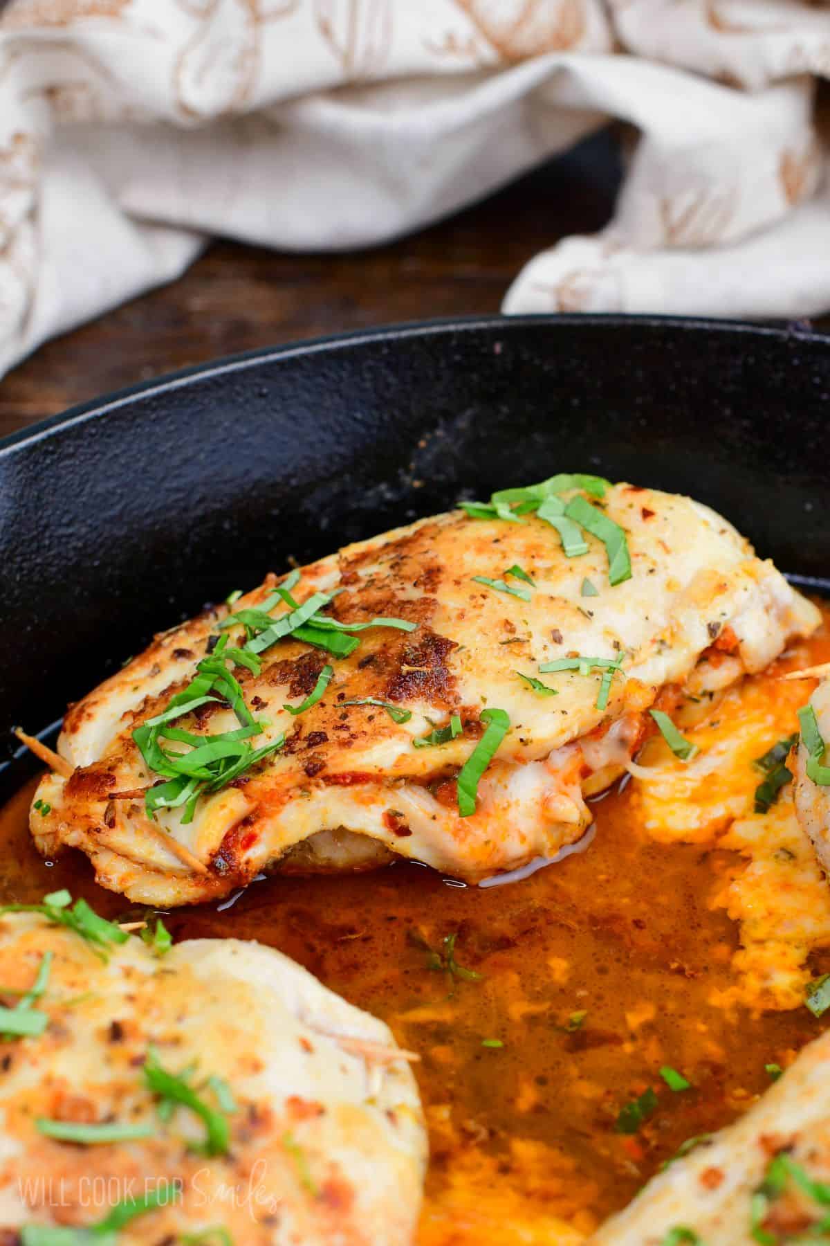 Cooked sun dried tomato pesto stuffed chicken in a cast iron skillet with melted cheese and fresh basil.