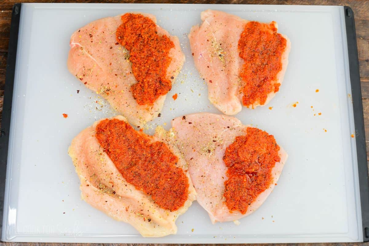 Butterflied chicken breasts spread with sun dried tomato pesto and seasoned on a cutting board.
