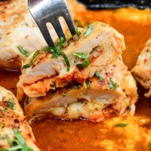 Sun dried tomato pesto stuffed chicken with melted fontina cheese, sliced open in a cast iron skillet with a fork.