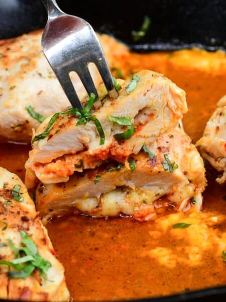 Sun dried tomato pesto stuffed chicken with melted fontina cheese, sliced open in a cast iron skillet with a fork.