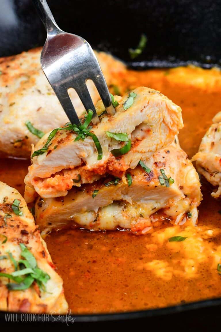 Sun dried tomato pesto stuffed chicken with melted fontina cheese, sliced open in a cast iron skillet with a fork.