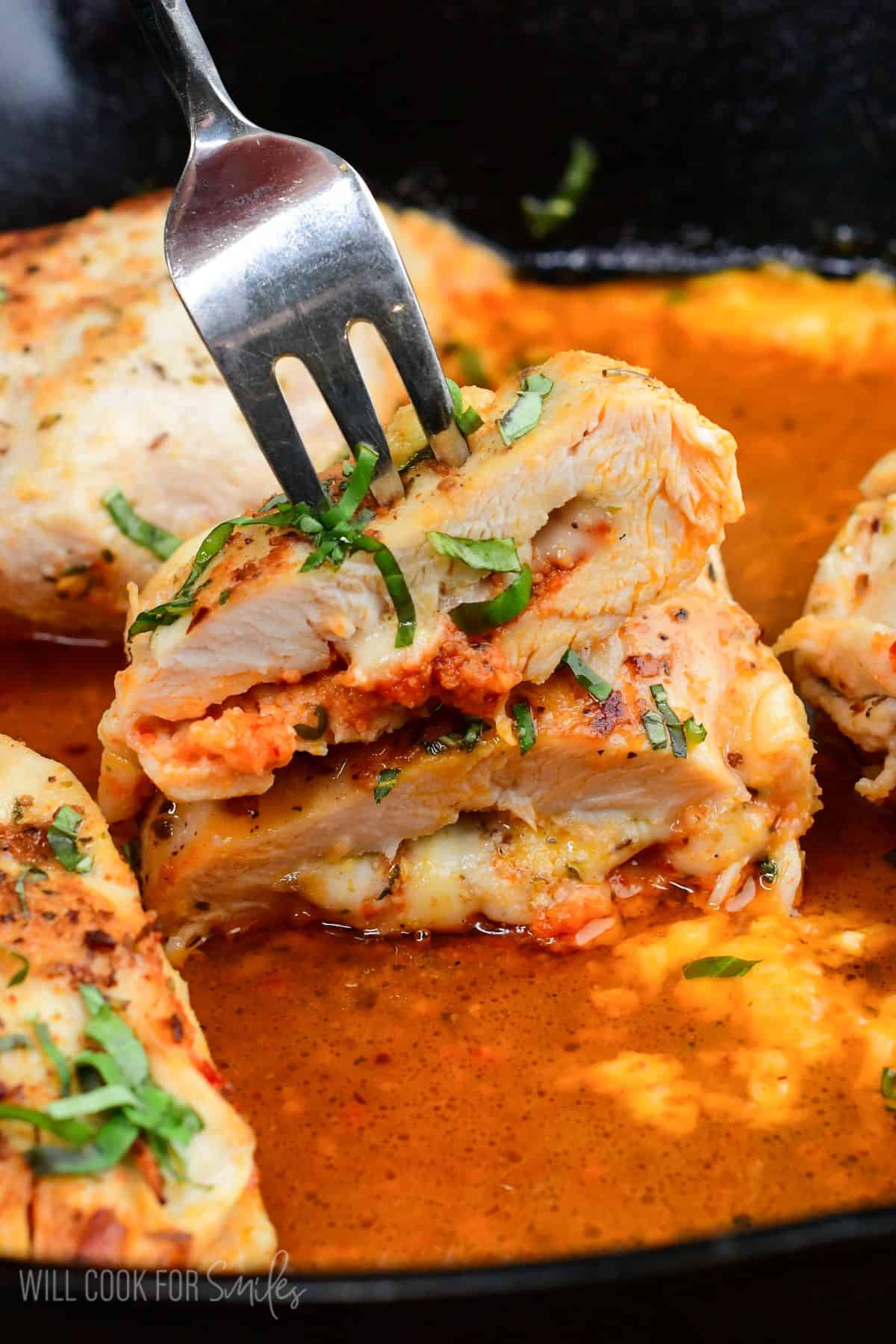 Sun dried tomato pesto stuffed chicken with melted fontina cheese, sliced open in a cast iron skillet with a fork.