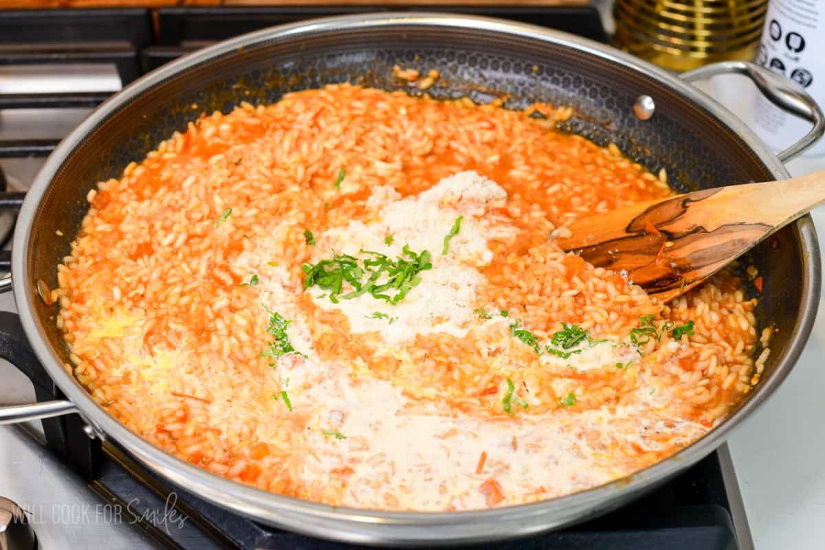 adding cream, parmesan cheese, and basil to the risotto as it's cooking in the pan.