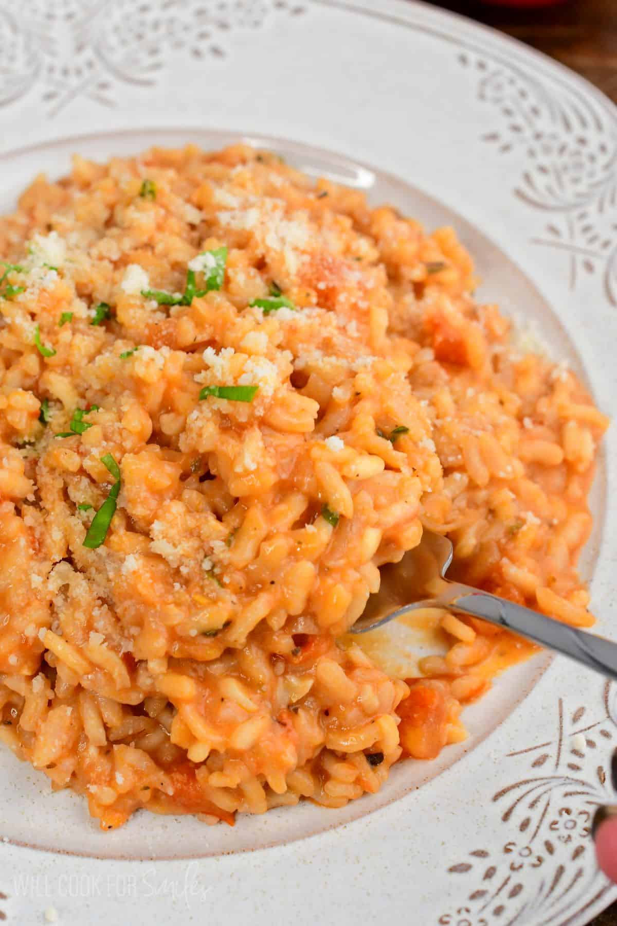 scooping out some creamy tomato risotto from the pate with a fork.