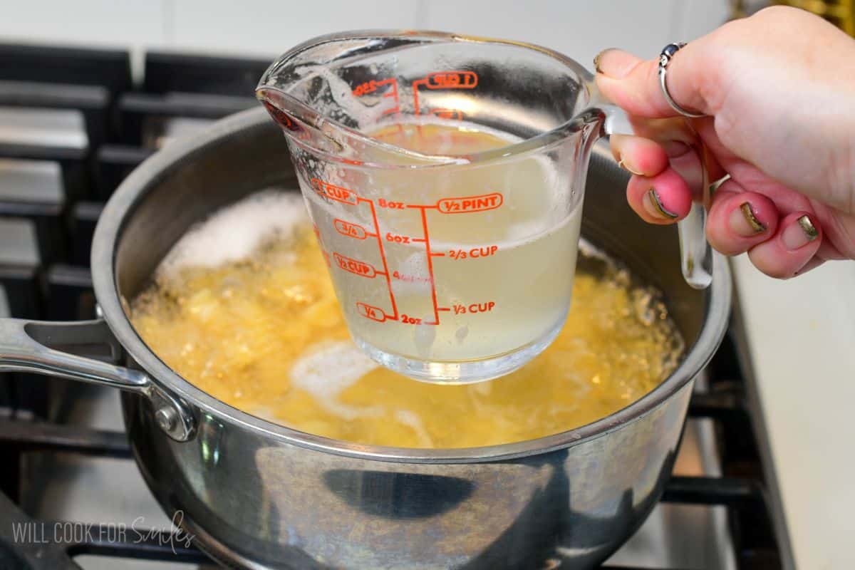 Measuring cup filled with reserved pasta cooking water held over a pot of boiling pasta.