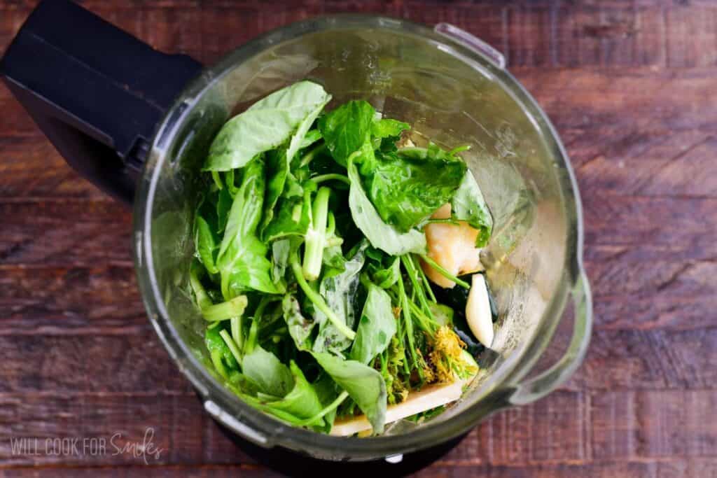 Fresh basil, garlic, Parmesan, and herbs in a blender ready to make homemade pesto.