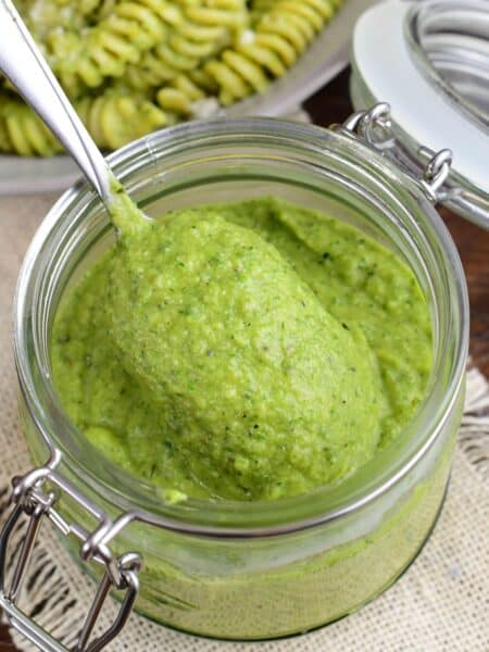 Spoonful of creamy homemade zucchini pesto scooped from a glass jar.