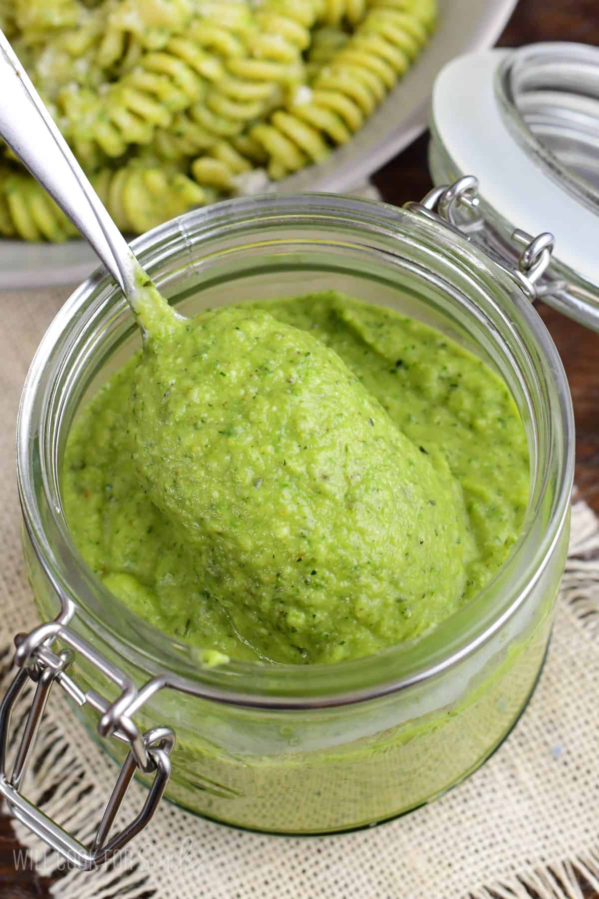 Spoonful of creamy homemade zucchini pesto scooped from a glass jar.