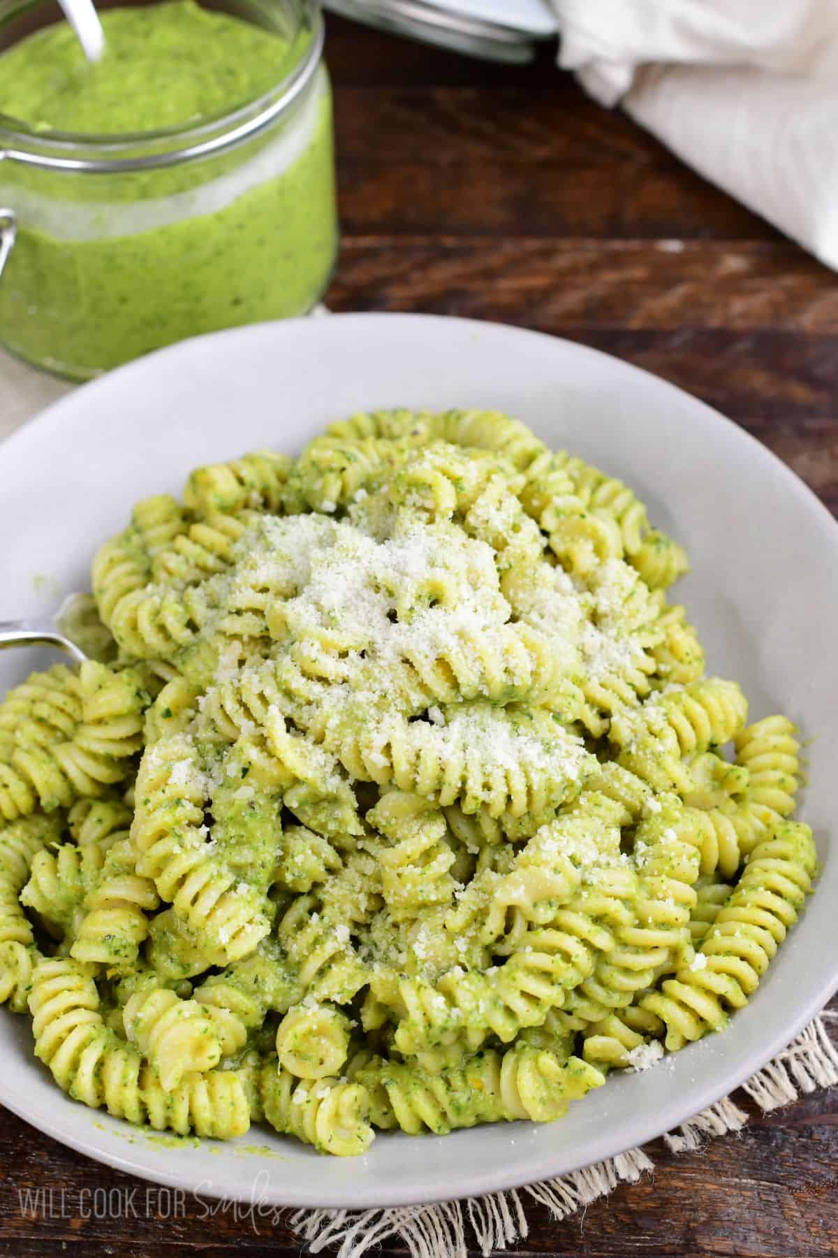 Zucchini pesto pasta topped with Parmesan, served in a bowl with a jar of pesto in the background.