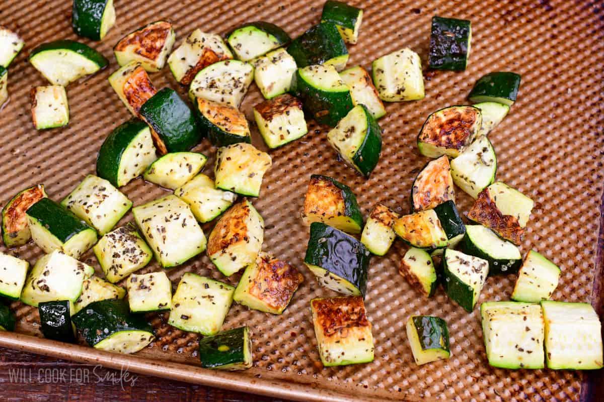 Roasted zucchini pieces seasoned with herbs and browned on a baking sheet.