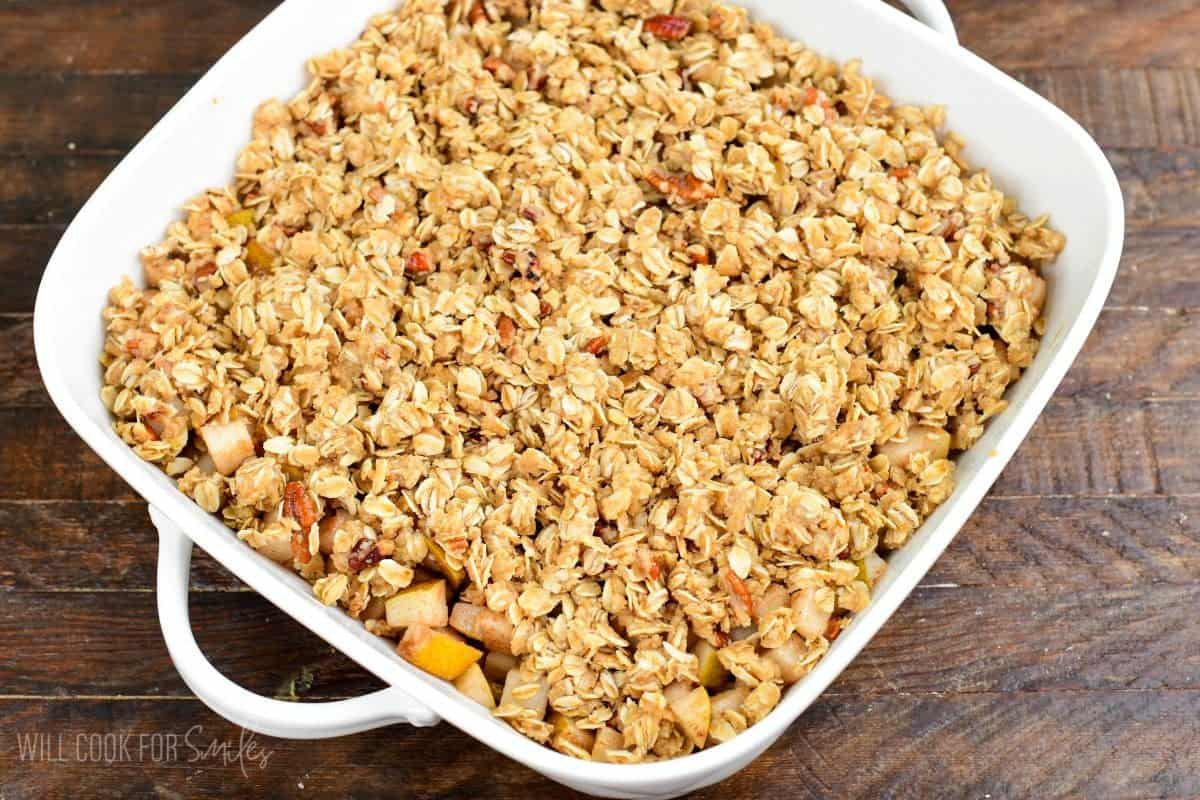 Pear crisp topped with an oat and pecan crumble in a baking dish, ready to bake.