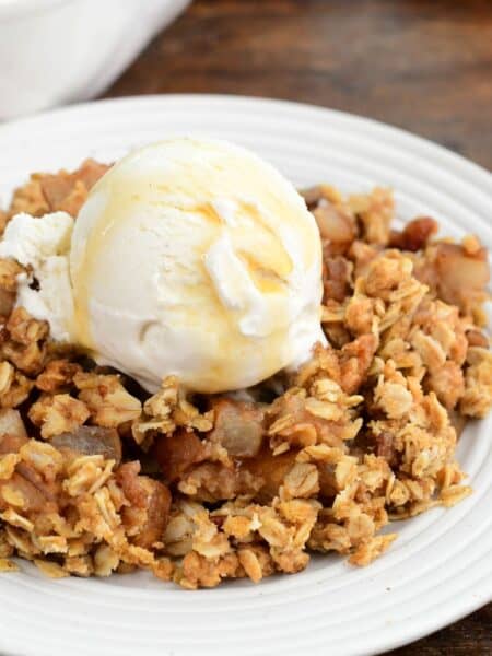 Asian pear crisp with a crunchy oat topping, vanilla ice cream, and maple syrup on a plate.