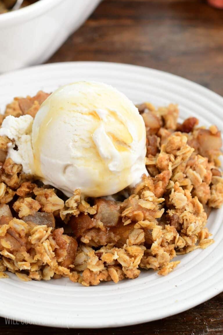 Asian pear crisp with a crunchy oat topping, vanilla ice cream, and maple syrup on a plate.