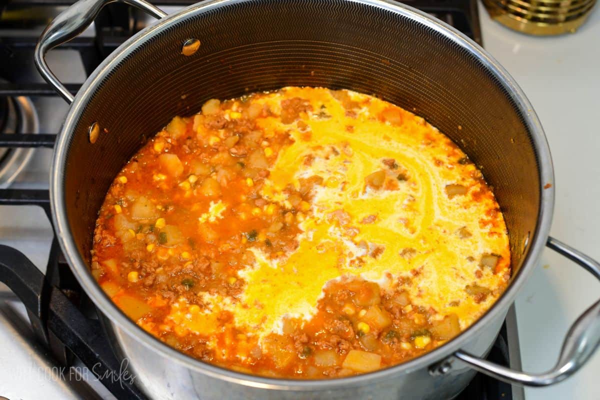 Cream and broth added to chorizo potato soup with potatoes, corn, sausage, and seasonings simmering in a pot.