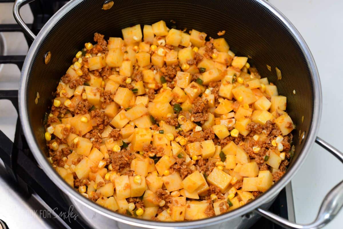 Diced potatoes, corn, chorizo, onions, and peppers cooking together in a large pot for chorizo potato soup.