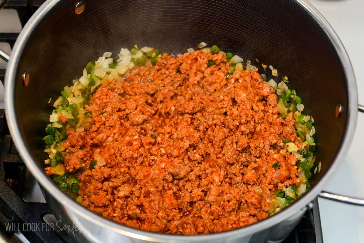 Chorizo cooking with chopped onions and green peppers in a large pot for chorizo potato soup.