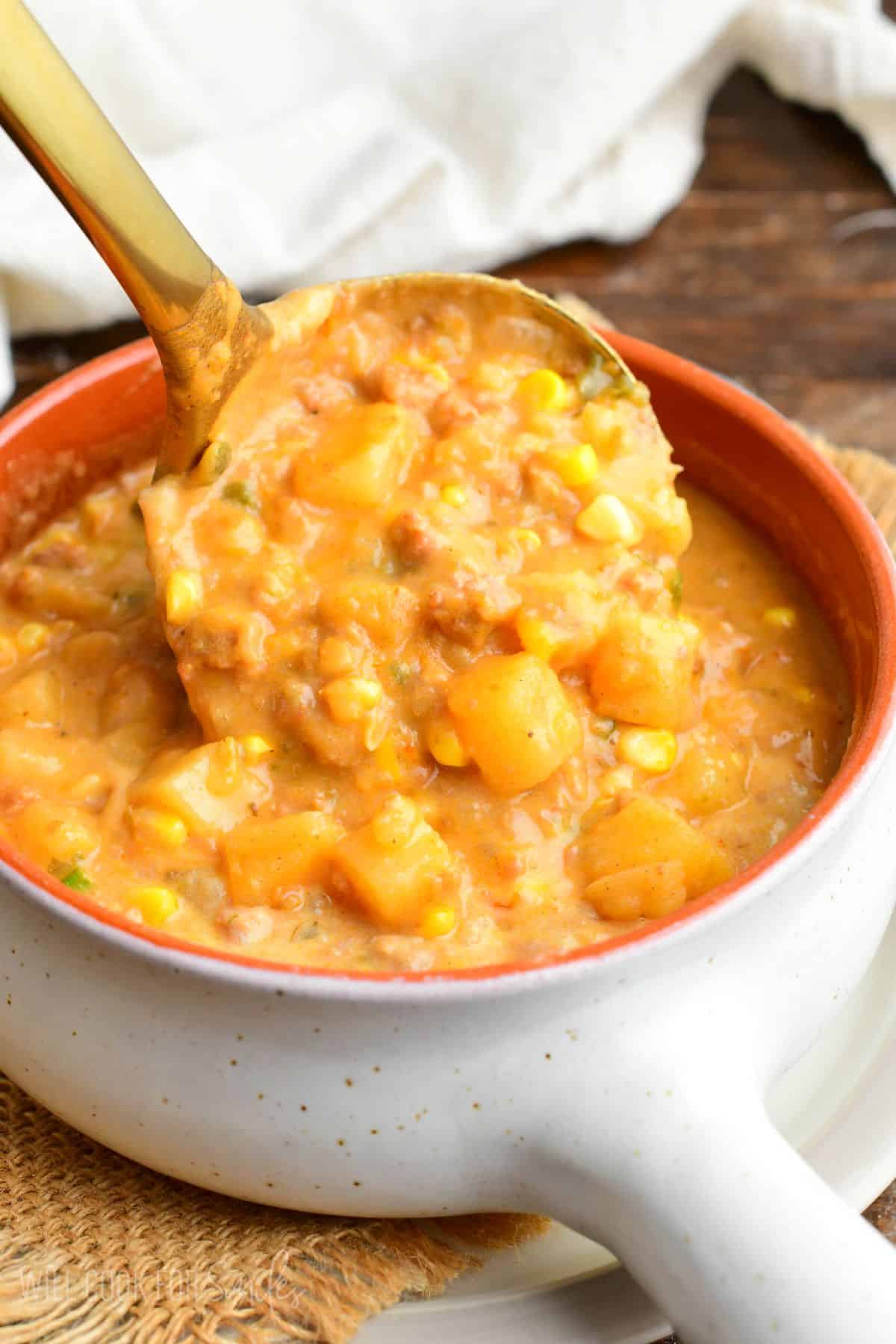 pouring in a ladle of creamy chorizo sausage potato soup into the bowl.