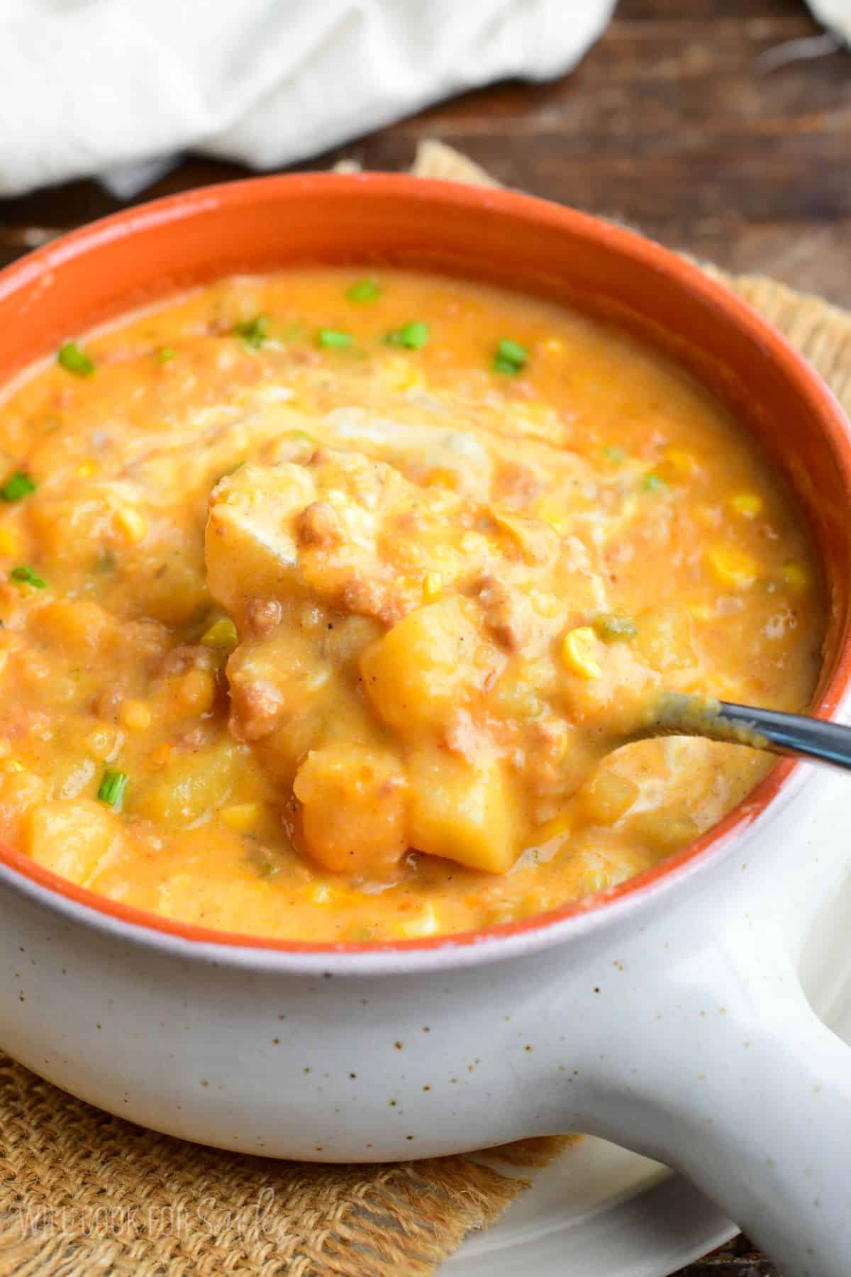Creamy chorizo sausage potato soup with tender potatoes and corn being scooped up with a spoon.