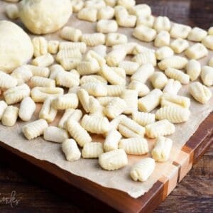 many homemade fresh uncooked pieces of gnocchi spread on parchment paper with some gnocchi dough too.