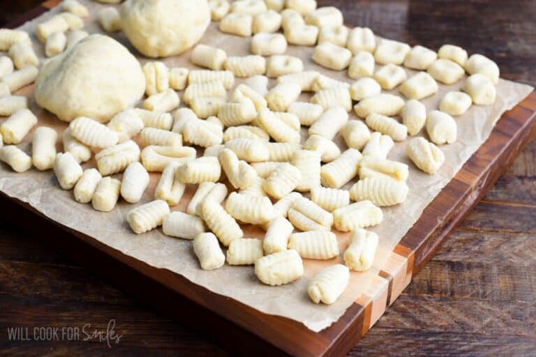many homemade fresh uncooked pieces of gnocchi spread on parchment paper with some gnocchi dough too.