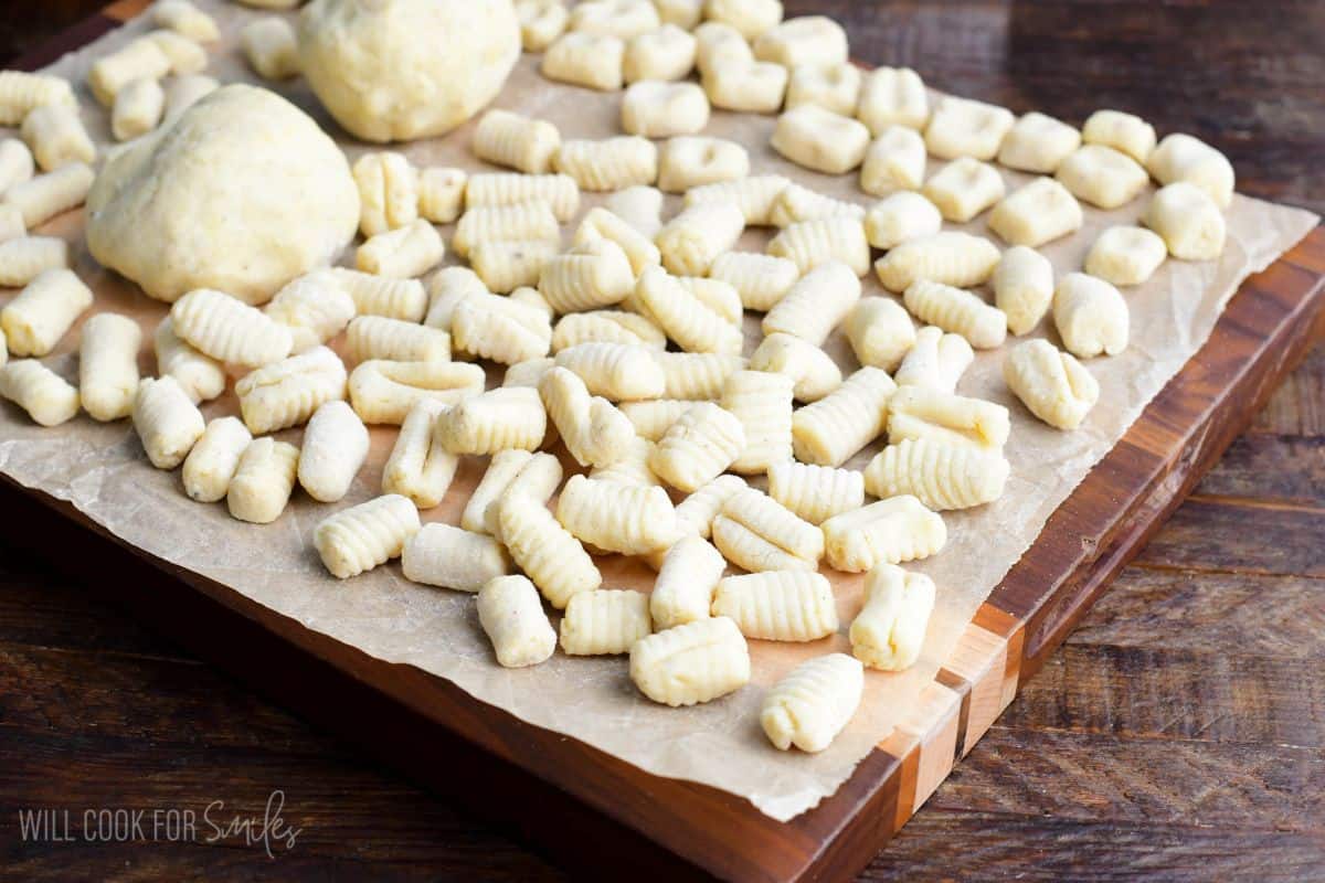 many homemade fresh uncooked pieces of gnocchi spread on parchment paper with some gnocchi dough too.