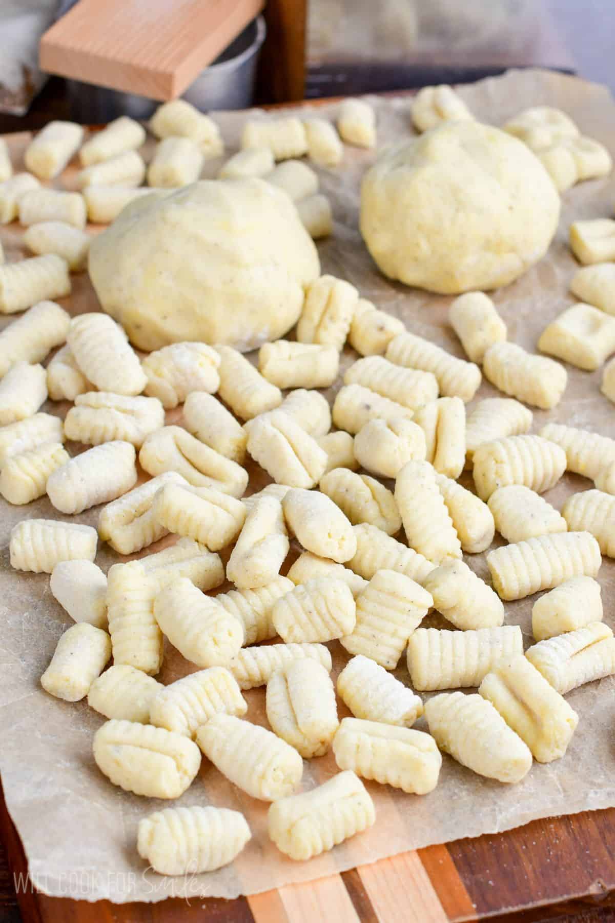 lots of fresh uncooked gnocchi spread on the cutting board with a couple dough rolls unrolled.