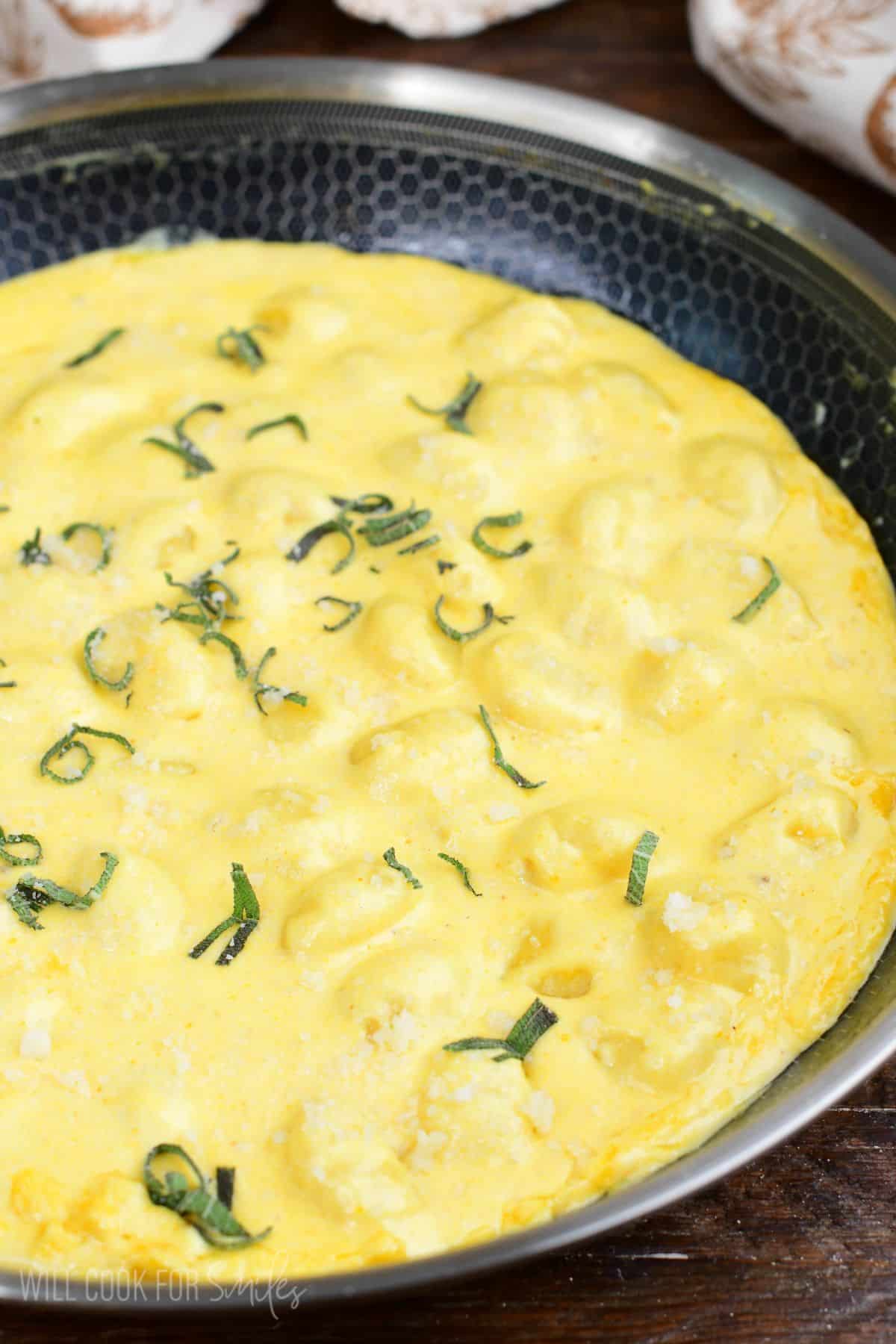 Creamy pumpkin Alfredo gnocchi topped with Parmesan and fresh sage in a skillet.