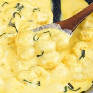 Creamy pumpkin Alfredo gnocchi with sage scooped onto a wooden spoon in the skillet.
