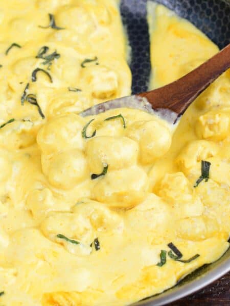 Creamy pumpkin Alfredo gnocchi with sage scooped onto a wooden spoon in the skillet.
