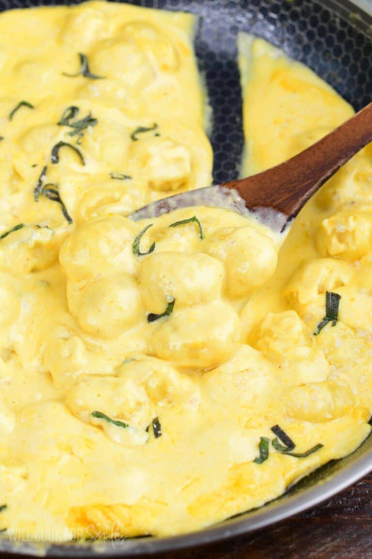 Creamy pumpkin Alfredo gnocchi with sage scooped onto a wooden spoon in the skillet.
