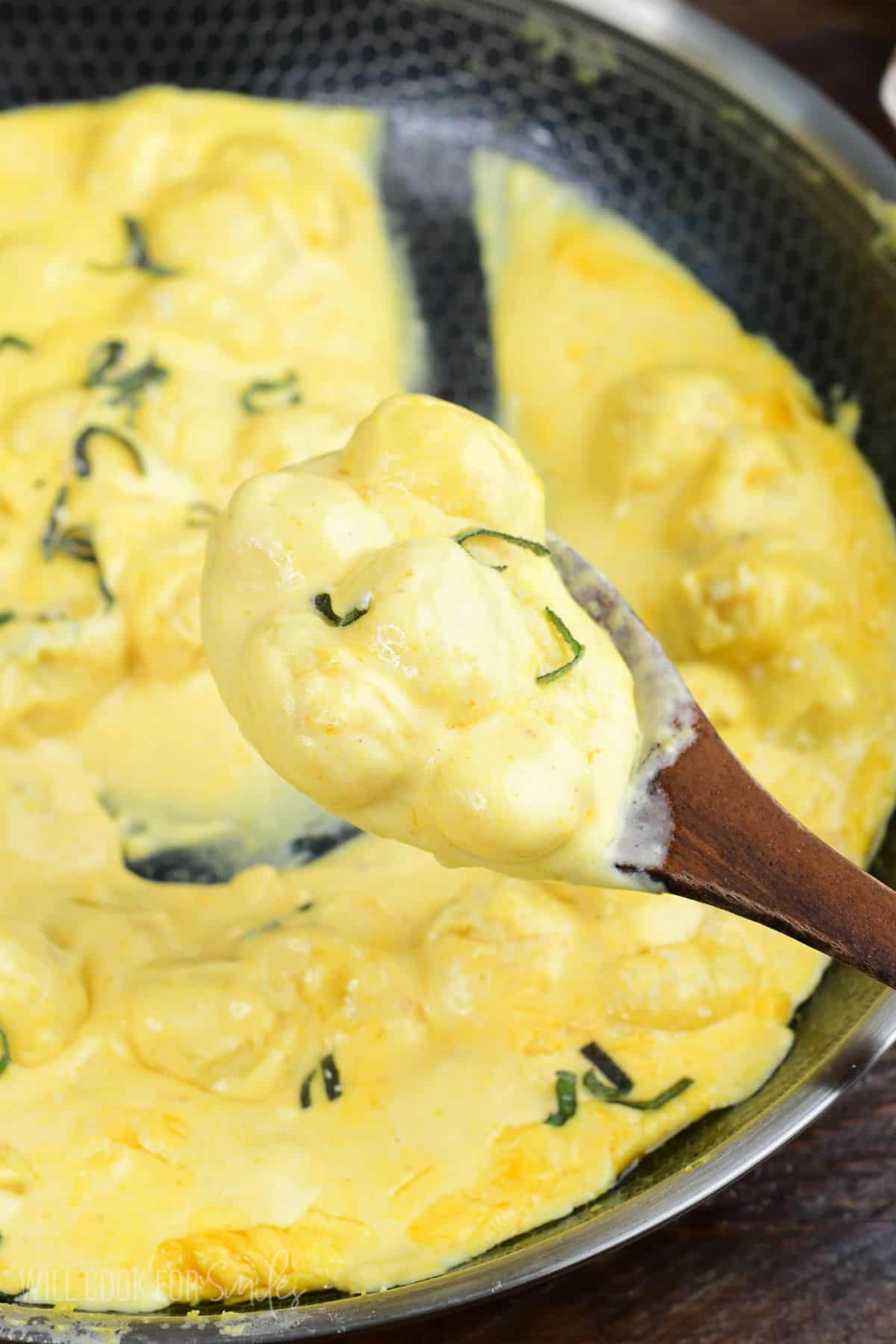 Creamy pumpkin Alfredo gnocchi with fresh sage scooped onto a wooden spoon.