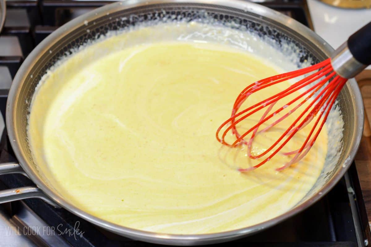 Creamy pumpkin Alfredo sauce being whisked in a skillet until smooth and combined.
