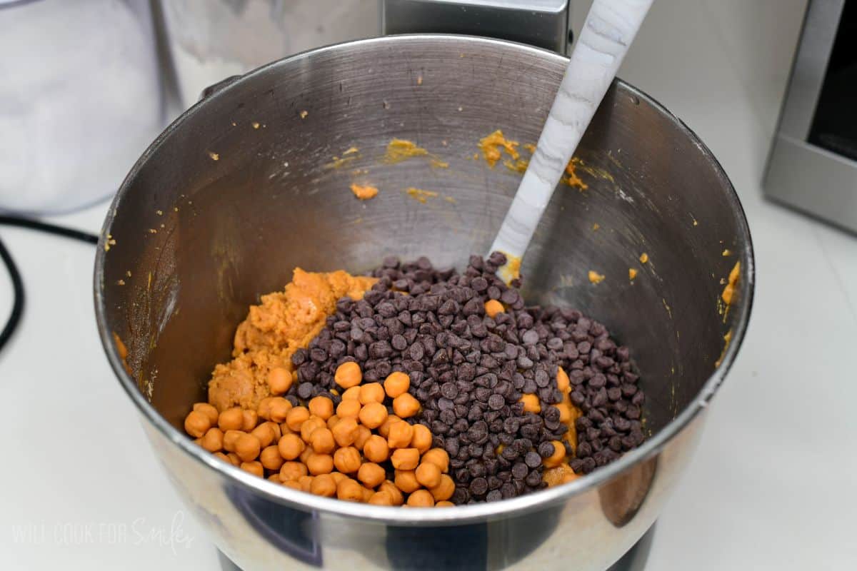 Peanut butter cookie dough topped with chocolate chips and caramel bits in a mixing bowl.