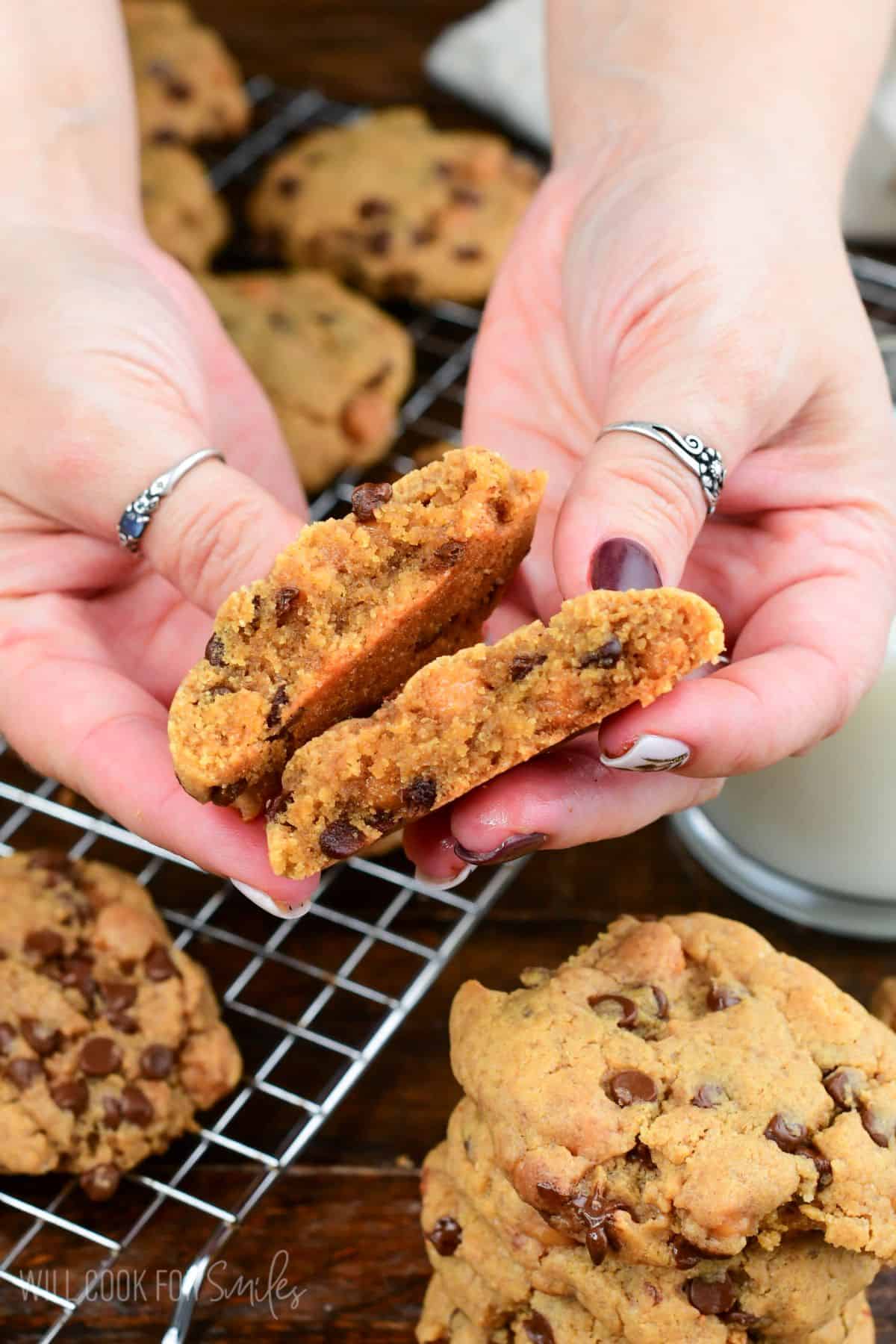Holding a peanut butter cookie broken in half, showing a soft center filled with chocolate chips and caramel pieces.