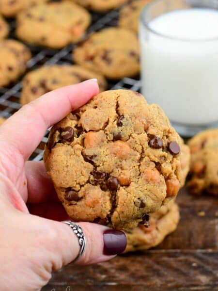 Holding a thick peanut butter cookie loaded with chocolate chips and caramel bits.