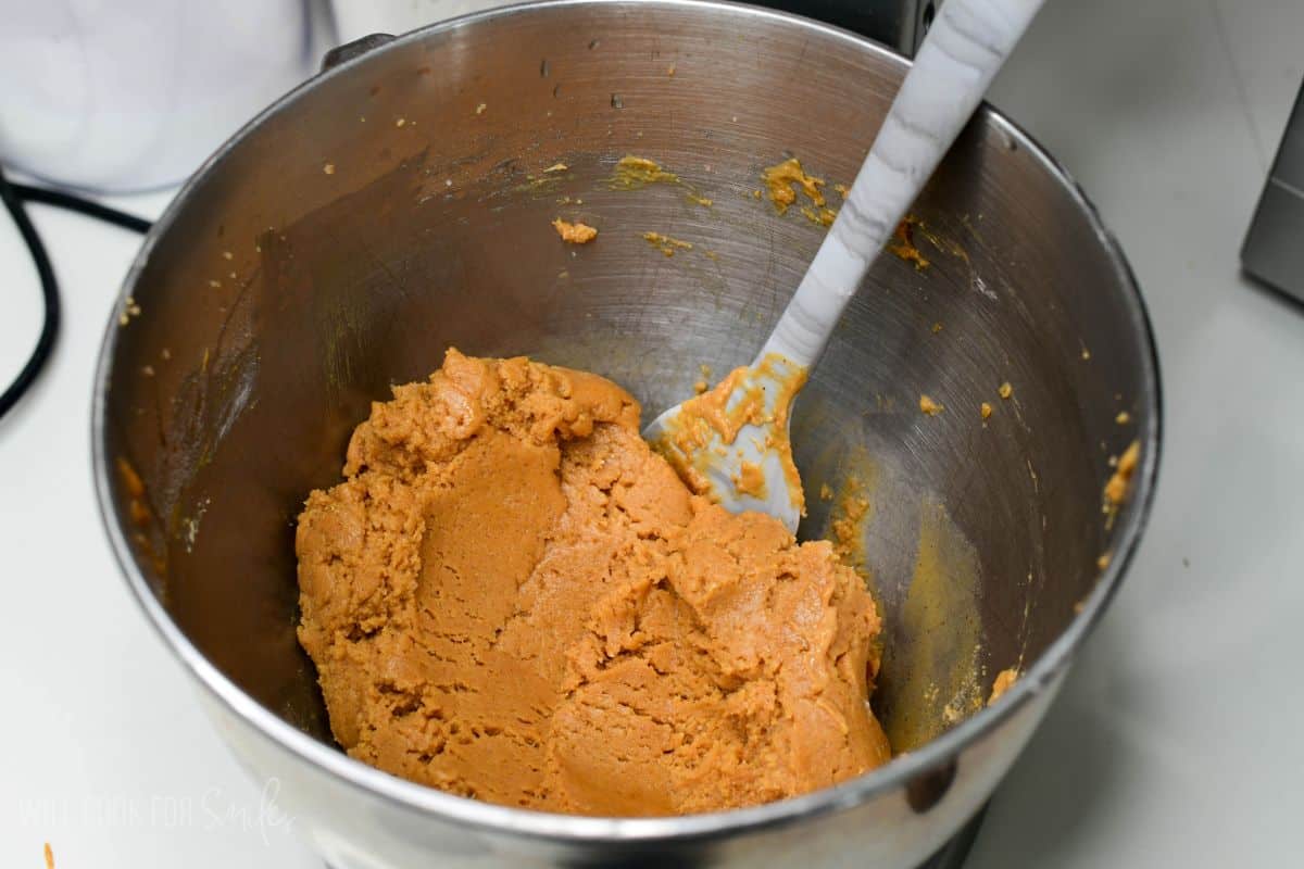 Peanut butter cookie dough mixed in a stand mixer bowl with a spatula.