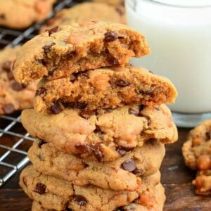 Stack of thick peanut butter cookies with chocolate chips and caramel bits, with one cookie split open on top.