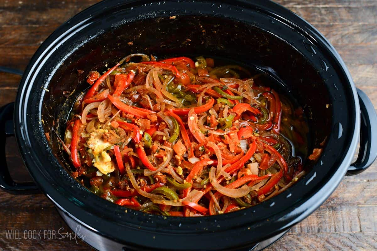 Cooked crockpot salsa chicken topped with softened red and green peppers, onions, and tomatoes in the slow cooker.