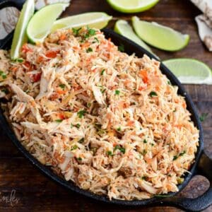 Crockpot salsa chicken with shredded chicken, peppers, and herbs in a cast iron skillet surrounded by lime wedges.
