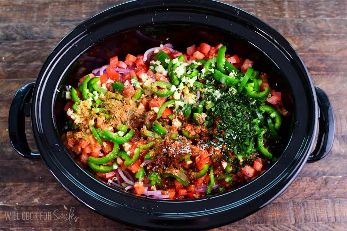 Crockpot salsa chicken ingredients with chopped tomatoes, green peppers, red onion, garlic, herbs, and spices.